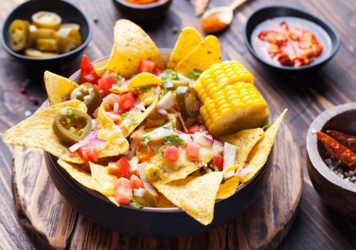 nachos,with,melted,cheese,sauce,,salsa,and,corn,cobs,in